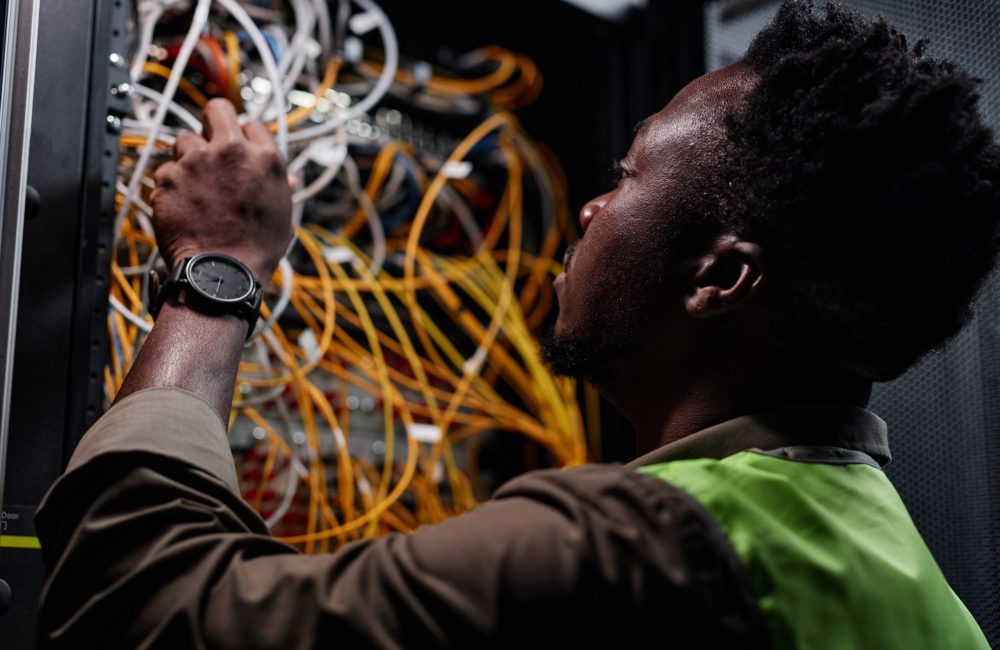 Close up of black man as network technician connecting cables and wires while repairing server in data center